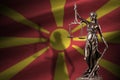 Macedonia flag with statue of lady justice and judicial scales in dark room. Concept of judgement and punishment