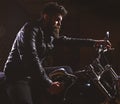 Macho, brutal biker in leather jacket riding motorcycle at night time, copy space. Man with beard, biker in leather