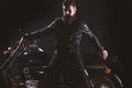 Macho, brutal biker in leather jacket stand near motorcycle at night time, copy space. Man with beard, biker in leather