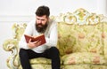 Macho on concentrated face reading book. Scandalous bestseller concept. Man with beard and mustache sits on baroque