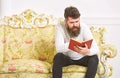 Macho on concentrated face reading book. Scandalous bestseller concept. Man with beard and mustache sits on baroque Royalty Free Stock Photo