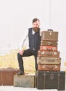 Macho elegant on disappointed face standing near pile of vintage suitcase. Man, butler with beard and mustache delivers