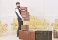 Macho, elegant porter on strict face carries pile of vintage suitcases. Butler and service concept. Man with beard and