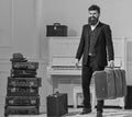Macho elegant on smiling face stands near pile of vintage suitcase, holds suitcase. Man, traveller with beard and
