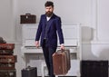 Macho elegant on strict face stands near pile of vintage suitcase, holds suitcase. Baggage delivery concept. Man