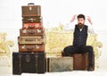 Macho elegant on surprised face sits shocked near pile of vintage suitcase. Luggage and relocation concept. Man, butler