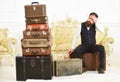 Macho elegant on tired face sits, exhausted at end of packing, near pile of vintage suitcases. Luggage and relocation