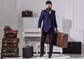 Macho stylish on strict face stands and carries big vintage suitcase. Man, traveller with beard and mustache with