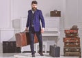 Macho stylish on strict face stands and carries big vintage suitcase. Man, traveller with beard and mustache with
