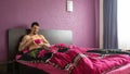 Macho tattoo muscular guy sitting in bed of the hotel, having breakfast with nude chest. Lonely Handsome man smiling, holding bowl Royalty Free Stock Photo