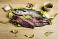 Mackerel fresh fish on lettuce leaves next to bay leaves, a few pieces of lemon, a bowl of oil and some spices on a wooden table Royalty Free Stock Photo