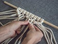 Macrame. Girl weaves macrame. White thread, female hand, grey background, close-up