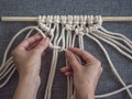 Macrame. Girl weaves macrame. White thread, female hand, grey background, close-up Royalty Free Stock Photo