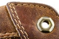 Macro background made of brown natural leather with white stitches all around, visible metal leathercraft eyelet.