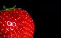 Macro close up of one single isolated ripe red strawberry with green leaves on black reflecting glass plate illuminated by studio Royalty Free Stock Photo