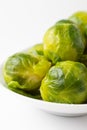 Macro closeup of green Brussels sprouts on white plate, white background, vertical Royalty Free Stock Photo