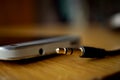 Macro detail of a metal headphone jack nearby the connector in the cellphone, on the wooden surface