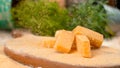 MACRO: Parmesan flakes fall on the cheese cubes on the wooden board. Royalty Free Stock Photo