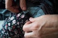 Macro elderly woman hands sewing on fabric, needle. Sew pants by old woman hand, seamstress at work with cloth fabric. Grandmother