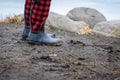Muddy buffalo plaid boots standing along rocky shoreline