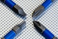 A macro image of 4 drill driver bits, 2 phillips head, a star driver and a square drive, on a steel industrial surface in an X