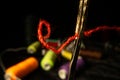 Needle eye threaded with piece of red thread on black background with colored spools of thread. Steel tailor needle with Royalty Free Stock Photo