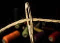 Needle eye threaded with piece of white thread on black background with colored spools of thread. Steel tailor needle Royalty Free Stock Photo