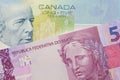 A pink and purple five real bank note from Brazil paired with a blue five dollar bill from Canada.