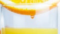 Macro image of juice droplet on side of orange half falling in glass with fresh juice