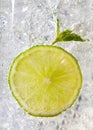 Macro photo of a piece of lime and mint leaf in a glass with ice and bubbles. Cold summer drink concept Royalty Free Stock Photo