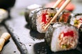 Macro shot of eating sushi roll in Japanese restaurant with chopsticks closeup. Taking portion of sushi rolls with rice, fried sal