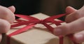 Macro shot of female hands tying red ribbon bow on craft paper gift box Royalty Free Stock Photo