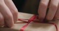 Macro shot of female hands tying red ribbon bow on craft paper gift box Royalty Free Stock Photo