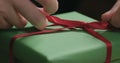 Macro shot of female hands tying red ribbon bow on green paper gift box Royalty Free Stock Photo