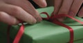 Macro shot of female hands tying red ribbon bow on green paper gift box Royalty Free Stock Photo