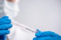 Macro shot of hands in blue protective gloves holds biological tube with label covid-19 on white background. Research and