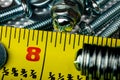 A Macro shot of the head of a small stainless steel bolt on a pile of washers, nuts and bolts, with a bright yellow tame measure Royalty Free Stock Photo