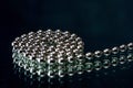 Macro shot of a spiraled beaded chain, on a dark reflecting background