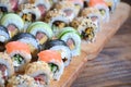 A macro shot of a sushi set of many rolls is located on a wooden cutting board on a table in the kitchen of a sushi bar. A tradit