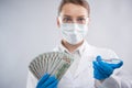 Macro shot view of microbiologist in protective gloves and face mask holds biological tubes with covid-19 vaccine and money on