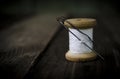 Macro of a spool of white thread and a needle with black sewing thread