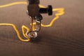 macro view on needle and foot of an embroidery machine stitching a golden ox symbol on brownish shiny olive fabric