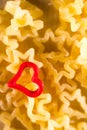 Macrophotography of a red heart on the background of curly pasta