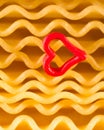 Macrophotography of a red heart on the background of curly pasta