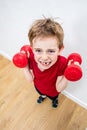 Mad frowning boy with loose tooth raising dumbbells with effort