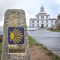 Sign of the Camino de Santiago and Finisterre Lighthouse in the background. In the light of day, in a sky with clouds. Galicia,
