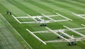 Gardeners tending a soccer field grass while large ultraviolet light devices help to care for it