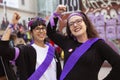 Two young women dressed in scarves and violet sash raise their fists and smile during the manifestation of Women`s Day