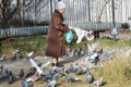Magadan, Russia - October 17, 2019. Old lady feeding pigeons on the street