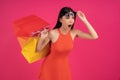 Mage of a beautiful shocked young asian woman posing isolated over pink wall background holding shopping bags. dressed in orange